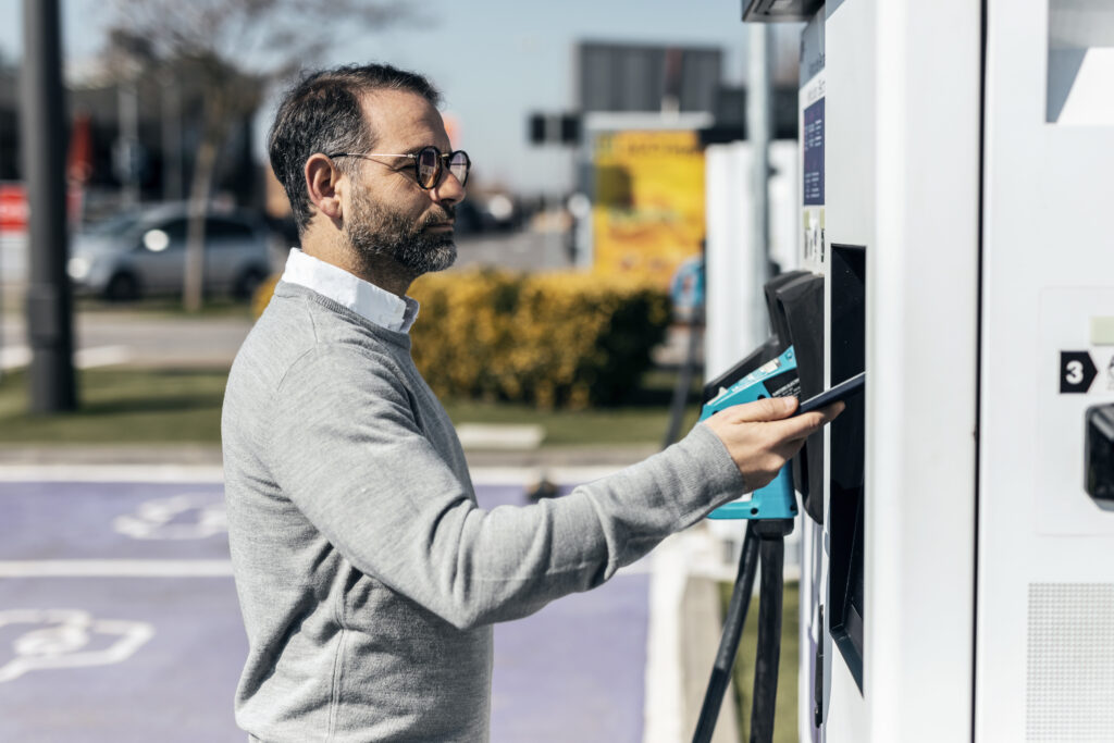 EV Charging Payments: Man paying through smart phone at car charging station